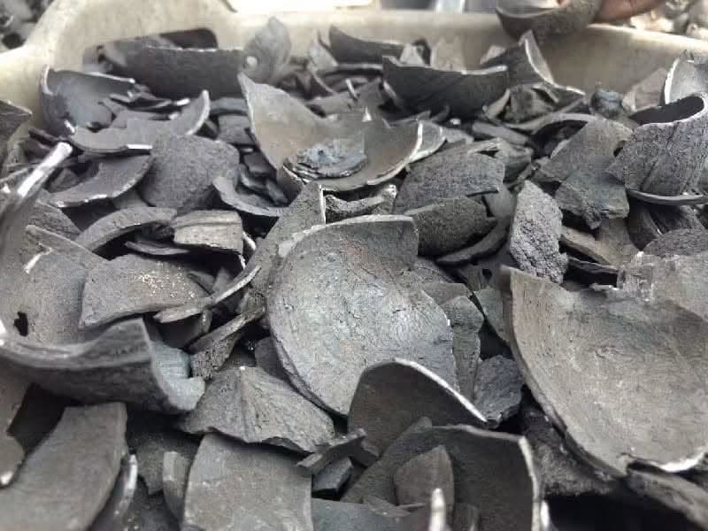 Curved lumps of coconut shell charcoal clustered on a pale concrete surface